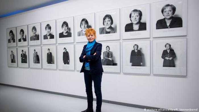 Herlinde Koelbl stands in front of portraits of Angela Merkel