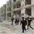 Policiais e outros homens caminham por cidade do Oriente Médio em ruínas