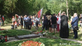 Grupa osób na cmentarzu z polskimi flagami