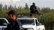 A policeman holding a gun stands on a police truck A policeman holding a gun stands on a police truck