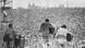 Richie Havens sitzt mit Gitarre auf der Bühne in Woodstock auf einem Barhocker, von hinten gesehen, sein Rücken verschwitzt, links ein Percussionist, rechts ein weiterer Gitarrist Richie Havens sitzt mit Gitarre auf der Bühne in Woodstock auf einem Barhocker, von hinten gesehen, sein Rücken verschwitzt, links ein Percussionist, rechts ein weiterer Gitarrist