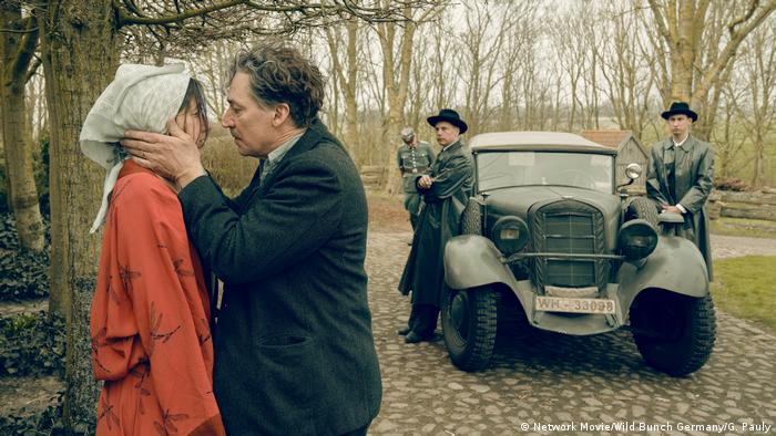Filmstill Deutschstunde, Tobias Moretti als Max Ludwig Nansen und Joanna Wokalek als Ditte beim Abschiedskuss. Im Hintergrund warten Polizisten bei einem Fahrzeug