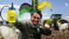 Fotomontagem com Bolsonaro com chapéu de bufão, segurando garrafa de agrotóxico, com boi e trator ao fundo Fotomontagem com Bolsonaro com chapéu de bufão, segurando garrafa de agrotóxico, com boi e trator ao fundo