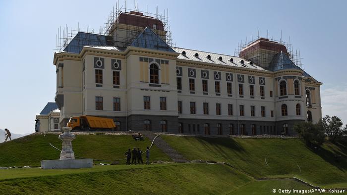 A grand building sits on a small hill with scaffolding on its roof