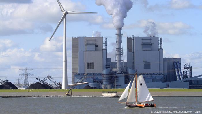 A sailboat passes by a wind turbine and power plant in the Netherlands