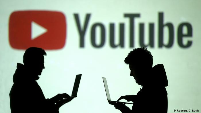 Фигуры двух мужчин, работающих с ноутбуками на фоне логотипа YouTube 