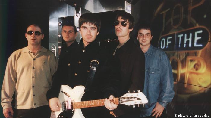 1997 photo of the five-member Britpop group, Oasis with guitarist Noel Gallagher holding a guitar