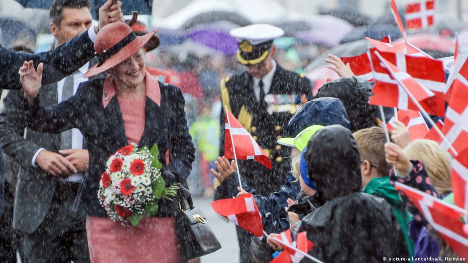 Königin Margrethe geht im dichten Regen an Fähnchen schwingenden Kindern vorbei