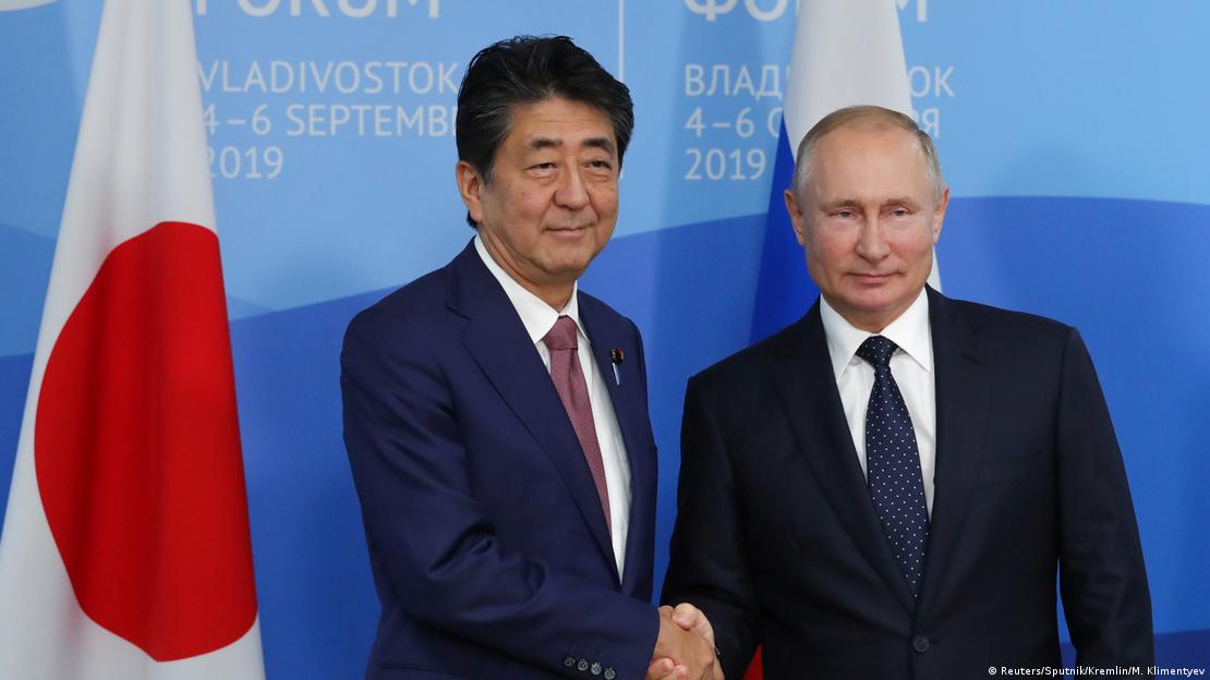 O ex-primeiro-ministro japonês Shinzo Abe e o presidente russo Vladimir Putin dão um aperto de mão enquanto posam para uma foto