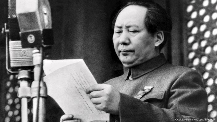 Mao Zedong reading from a document in front of microphones.