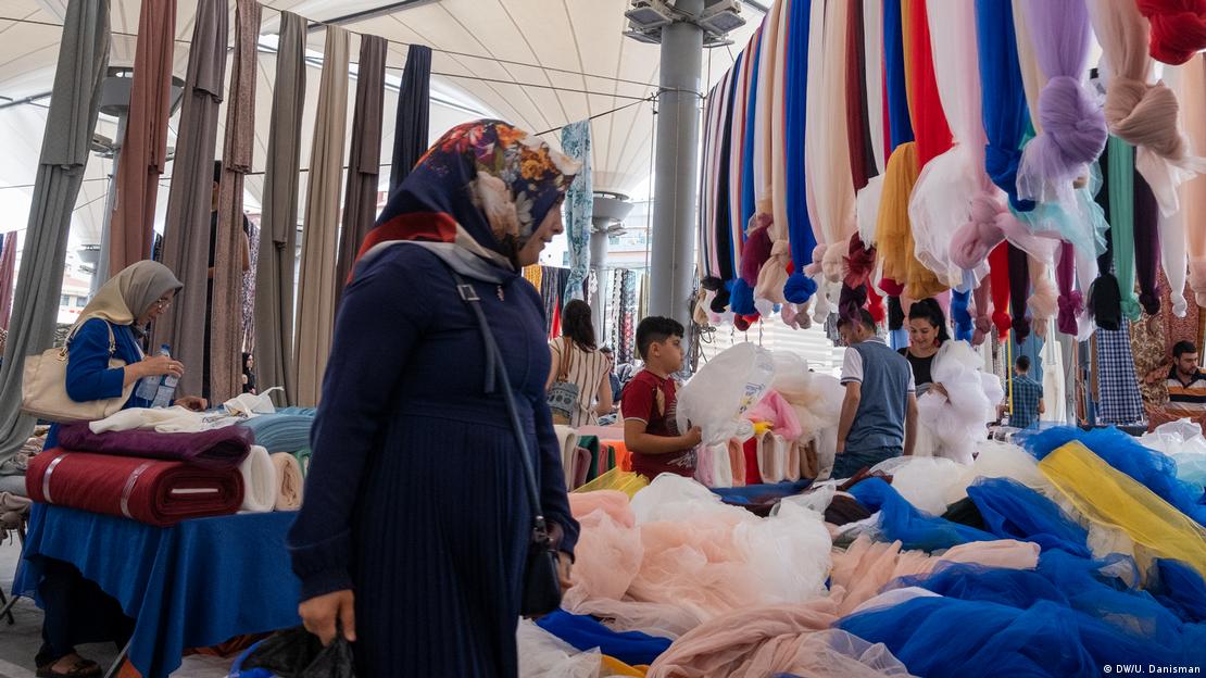 Türkiye'de bir pazarda tül tezgahı önünde duran başörtülü bir kadın, yandan görülüyor