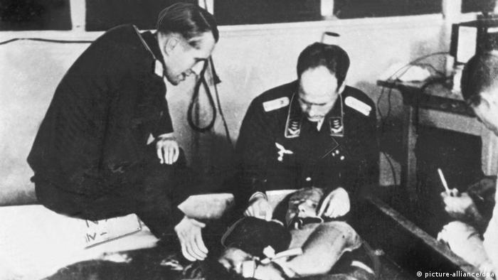 Zwei Männer in SS-Uniform beugen sich über ein Versuchsopfer bei einem Unterkühlungsversuch im KZ Dachau