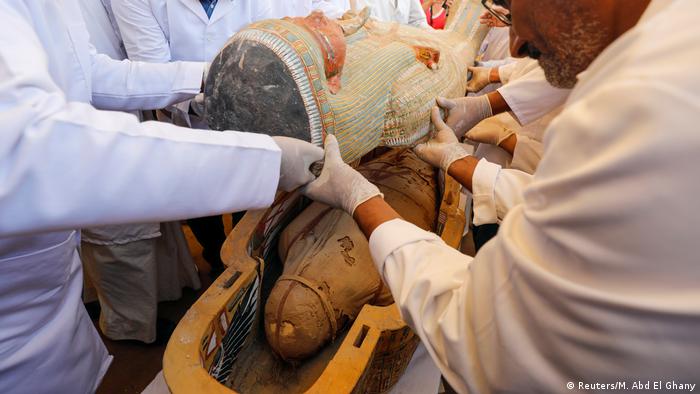 Hombres destapan la parte superior de un sarcófago egipcio.
