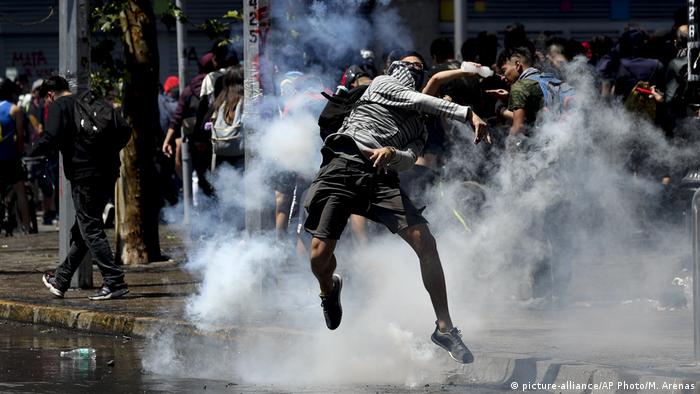A protester returns a tear gas cannister to police in Santiago, Chile