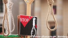 Bei einer Aktion gegen Folter und Todesstrafe im Iran vor dem Brandenburger Tor in Berlin hängen am 31.03.2017 symbolisch Henkersschlingen von einem Galgen. Daneben ist ein Schild mit einer Rose, einer Schlinge und der Aufschrift Stop zu sehen. Foto: Wolfram Steinberg/dpa | Verwendung weltweit