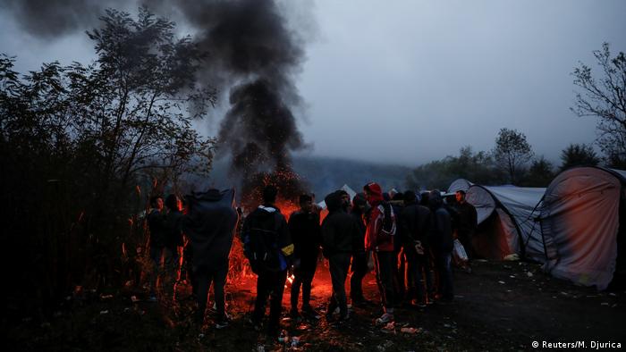 A group of people huddles in front of a fire, thick black smoke billowing (Foto: Reuters/M. Djurica)