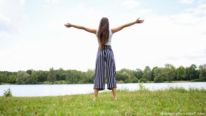 Woman standing out in a field in front of a lake with her arms open wide.
