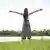 woman stands on grass, arms stretched out wide