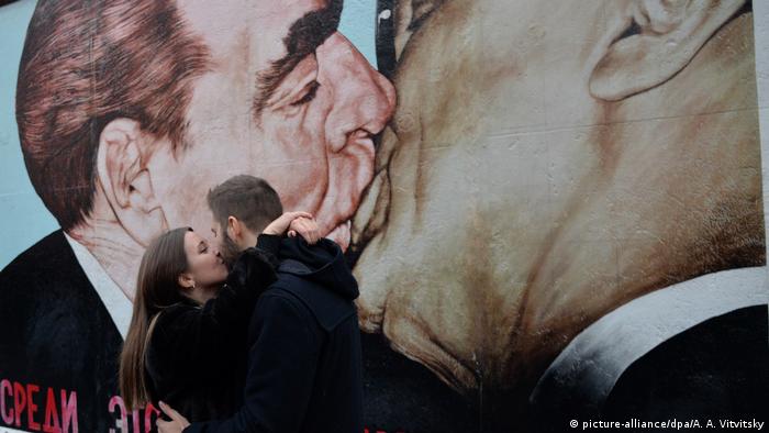A couple kiss in front of the My God, Help Me to Survive This Deadly Love mural