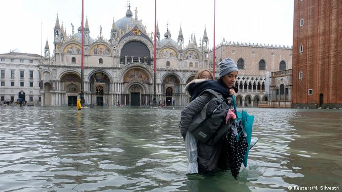 Eine Frau trägt ihr Kind Huckepack über den überfluteten Markusplatz
