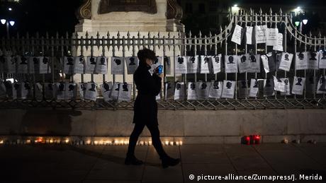 Woman walking past placards hung up on gate at night (picture-alliance/Zumapress/J. Merida)