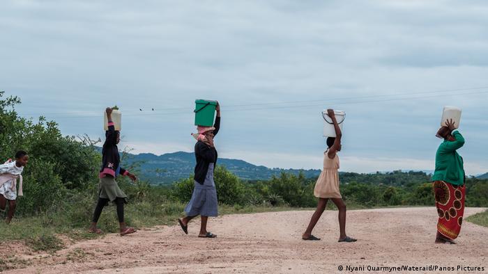 Four people in colorful clothes carry water containers on their head 