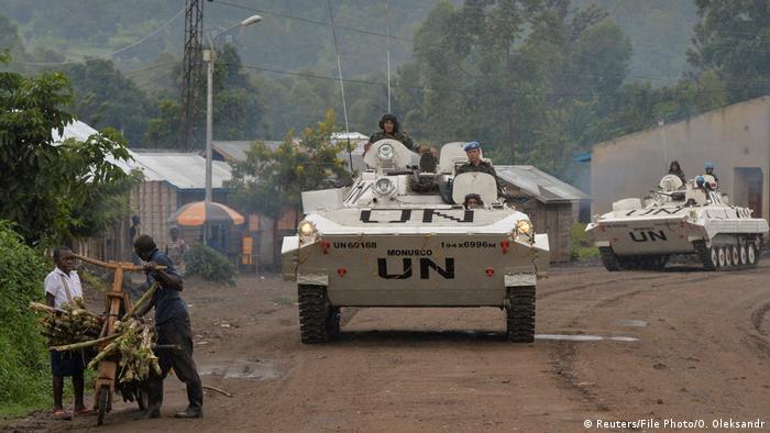 Congolese men push their makeshift bicycle past peacekeepers from India serving, in MONUSCO