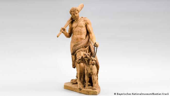 Στην ελληνική μυθολογία ο Κέρβερος αντιπροσωπεύει τον φύλακα του Άδη και έχει συνήθως τη μορφή ενός σκύλου με τρία κεφάλια. Ο Ηρακλής χρησιμοποιώντας μόνο τη δύναμη των χεριών του αιχμαλώτισε και μετέφερε τον Κέρβερο στον Ευρυσθέα, ο οποίος όμως από τον φόβο του τον έστειλε πίσω στον Άδη. Το πήλινο αυτό γλυπτό φιλοτεχνήθηκε το 1779 από τον Γερμανό καλλιτέχνη Ρόμαν Άντον Μπος. 