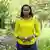 Sandrah Twinoburyo, Eco Africa presenter, in a yellow shirt surrounded by green leaves. 