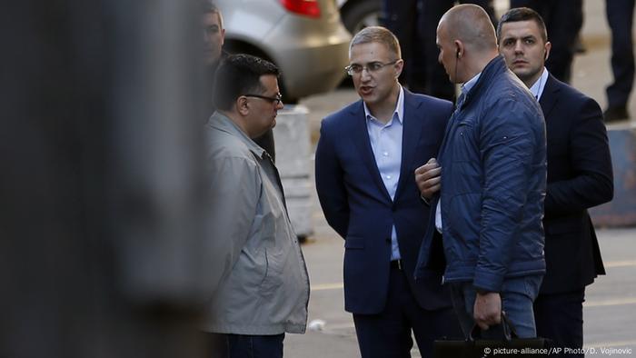 A man accompanied by two security officials talks to another man