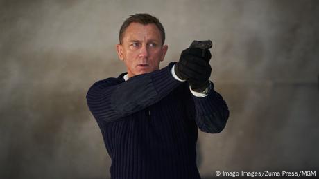 Daniel Craig hält in seiner Rolle als James Bond mit schwarzem Rollkragenpullover eine Pistole in der Hand und zielt.