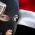 Masked fighter in front of the flag of Yemen