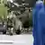 Im Vordergrund steht eine Frau, die in eine blaue Burka verhüllt ist. Im Hintergrund stehen Soldaten um ein Militär-Fahrzeug herum und beobachten die Frau. Provinz Herat (Archivfoto: dpa)