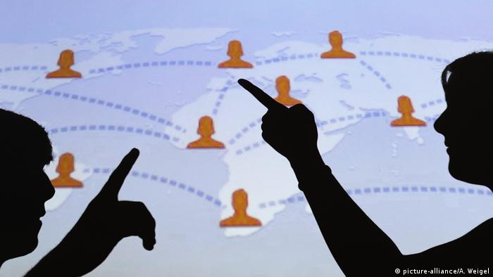 Two shadows gesture in front of a world map covered in interconnected Facebook logos