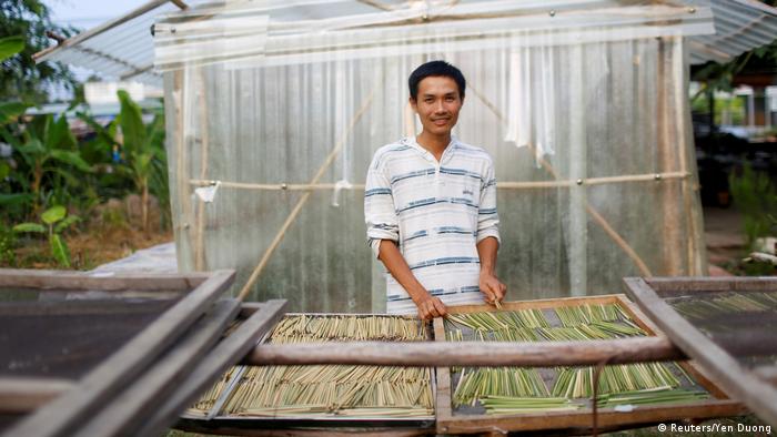 Tran Minh Tien stands behind a drying rack filled with grass straws. (Reuters/Yen Duong)