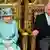 The queen of the UK sits in a green hat and jacket on a golden throne next to the Prince of Wales on the right