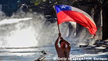 A demonstrator flutters a Chilean flag as a riot police water cannon sprays during a protest against Chilean President Sebastian Pinera's government in Santiago, on December 20, 2019. - Pinera promised support for victims of human rights violations by security forces during protests in Chile, and a firm commitment to achieve truth and justice. (Photo by Martin BERNETTI / AFP) (Photo by MARTIN BERNETTI/AFP via Getty Images)