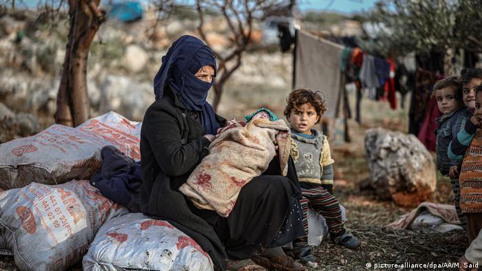 A woman sits with her children at a soil field in cold weather at Harbanush village, Idlib. Muhammed Said / Anadolu Agency