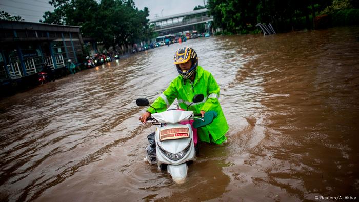 Un hombre con un casco verde brillante empujando su motocicleta a través de las aguas de la inundación en Yakarta.