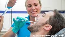 ILLUSTRATION - Eine Zahnaerztin zeigt einem Patienten am 15.08.2018 in einer Zahnarztpraxis in Oldenburg (Schleswig-Holstein) einen Zungenspatel zur Verbesserung der Mundhygiene (gestellte Szene). Foto: Christin Klose | Verwendung weltweit