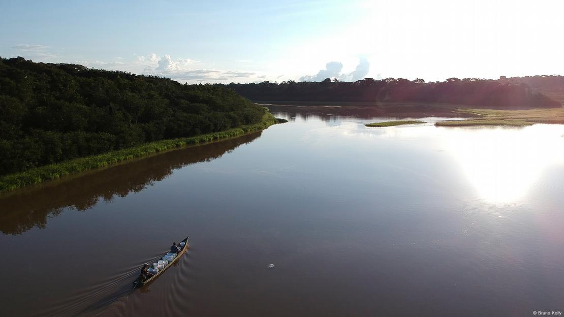 Vista aérea de rio em meio à floresta com pequeno barco nas águas