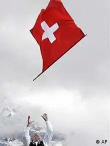 A man throws a Swiss flag in the air with a mountain backdrop