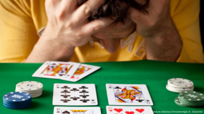 person holding his head, cards and poker chips on the table (picture-alliance/Chromorange/A. Gravante)