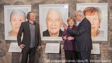 21.01.2020, Nordrhein-Westfalen, Essen: Der Künstler Martin Schoeller (l), der Holocaust-Überlebende Naftali Fürst und Bundeskanzlerin Angela Merkel (CDU) stehen in der Ausstellung «Survivors - Faces of Life after the Holocaust» in der Kokerei. Der Künstler Martin Schoeller hat 75 Jahre nach der Befreiung des Konzentrations- und Vernichtungslagers Auschwitz-Birkenau 75 Holocaust-Überlebende in Israel besucht und porträtiert. Die Arbeiten werden erstmalig präsentiert. Es ist ein gemeinsames Projekt der Stiftung für Kunst und Kultur Bonn mit der israelischen Holocaust-Gedenkstätte Yad Vashem. Foto: Rolf Vennenbernd/dpa | Verwendung weltweit