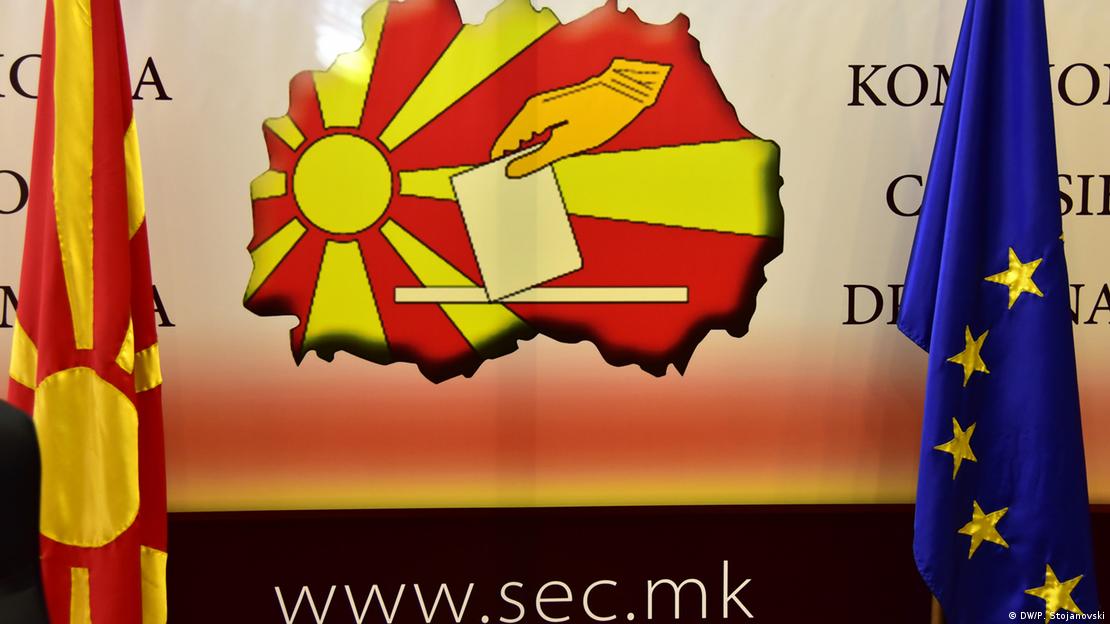 Големо лого на македонската Државна изборна комисија со картата на Македонија на која е пресликано македонското знами врс кое има нацртана рака како стаа ливче во симболична гласачка кутија. Македонското и знамето на ЕУ стојат пред логото/ Големо лого на македонската Државна изборна комисија со картата на Македонија на која е пресликано македонското знами врс кое има нацртана рака како стаа ливче во симболична гласачка кутија. Македонското и знамето на ЕУ стојат пред логото/