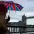 Duas pessoas andam sob um guarda-chuva com a bandeira britânica, próximo à Ponte de Londres