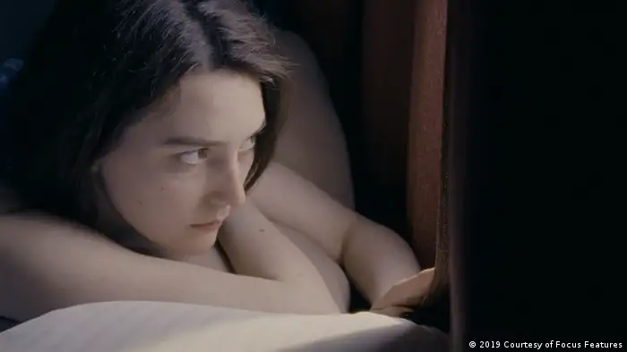 Eine junge Frau liegt auf einem Bett und schaut durch einen Vorhang aus dem Fenster (2019 Courtesy of Focus Features)