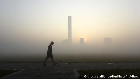 A lone man walking at dawn, smog covers the cityscape in the background