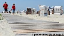 ARCHIV - Besucher gehen am 07.07.2016 über einen hölzernen Weg zum Strand der ostfriesischen Insel Spiekeroog (Niedersachsen). Foto: Ingo Wagner/dpa (zu dpa/lni: Guter Start in Hauptferienzeit - aber Hoffen auf besseres Wetter vom 17.07.2016) +++(c) dpa - Bildfunk+++ | Verwendung weltweit