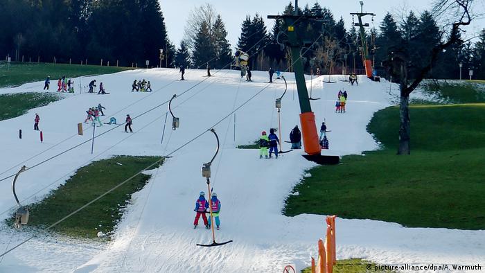 People skiing on slopes that do not have enough snow in Fischen im Allgäu, Germany